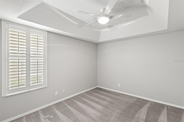 carpeted spare room featuring a ceiling fan, a tray ceiling, visible vents, and baseboards