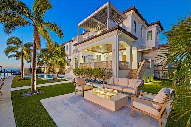 view of patio / terrace with a balcony, stairway, a fenced in pool, and an outdoor living space with a fire pit