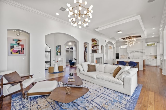 living room featuring light wood-style floors, visible vents, ornamental molding, and an inviting chandelier