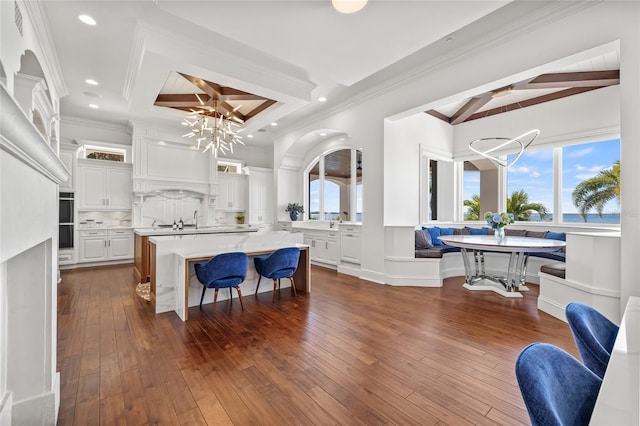 kitchen with backsplash, a kitchen island with sink, beam ceiling, light countertops, and a notable chandelier