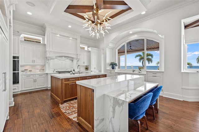 kitchen featuring a kitchen island with sink, decorative backsplash, dark wood-style floors, an inviting chandelier, and crown molding