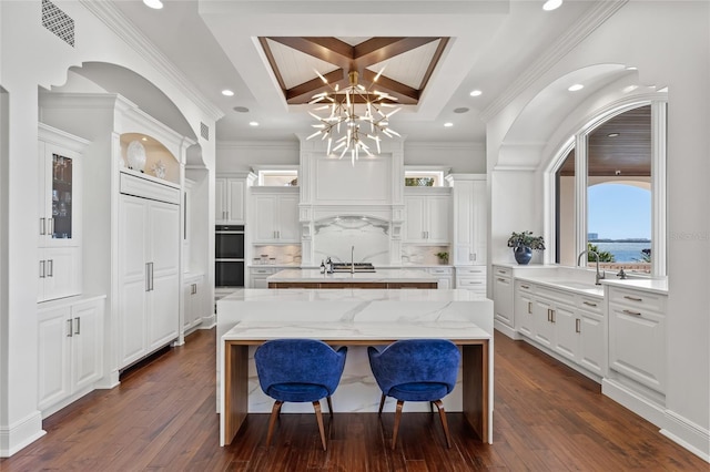 kitchen featuring a breakfast bar area, a kitchen island with sink, dobule oven black, coffered ceiling, and dark wood-style floors