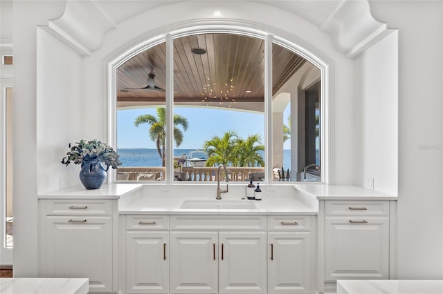 interior space with light countertops, white cabinetry, a sink, and a water view