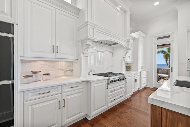 kitchen with decorative backsplash, dark wood-type flooring, crown molding, stainless steel gas stovetop, and white cabinetry