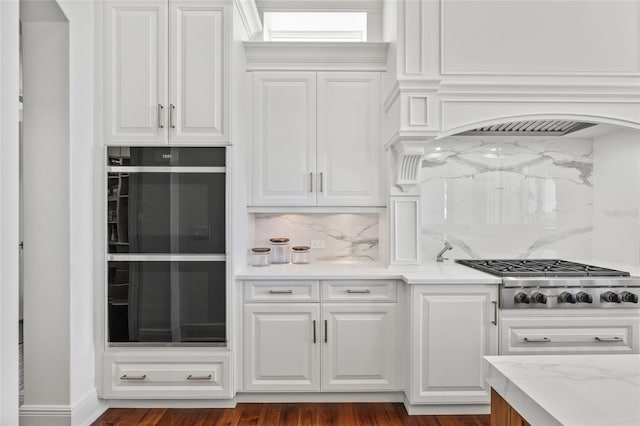 kitchen featuring tasteful backsplash, dobule oven black, stainless steel gas stovetop, white cabinets, and premium range hood