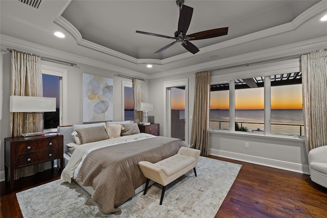 bedroom featuring wood finished floors, visible vents, baseboards, ornamental molding, and a tray ceiling