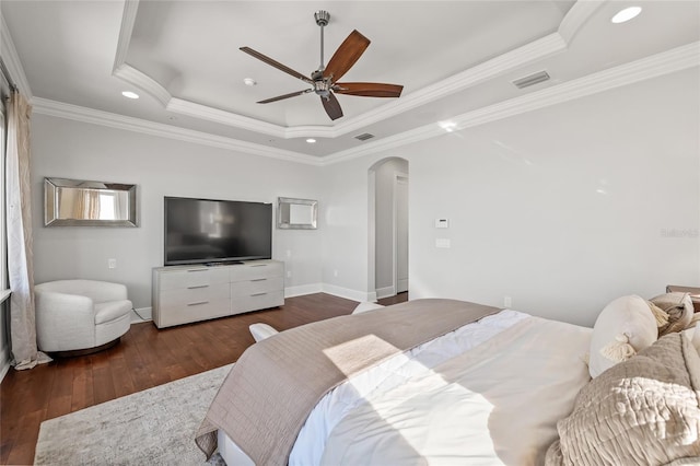 bedroom featuring visible vents, arched walkways, a raised ceiling, hardwood / wood-style flooring, and ornamental molding