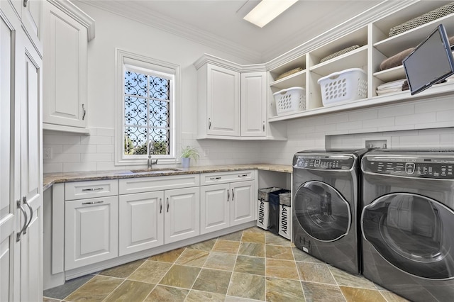 laundry area with crown molding, washing machine and clothes dryer, cabinet space, stone finish flooring, and a sink