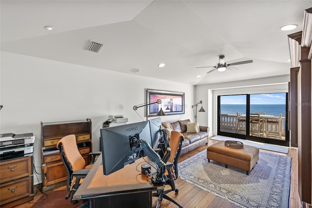 home office with dark wood-style floors, visible vents, vaulted ceiling, and a water view