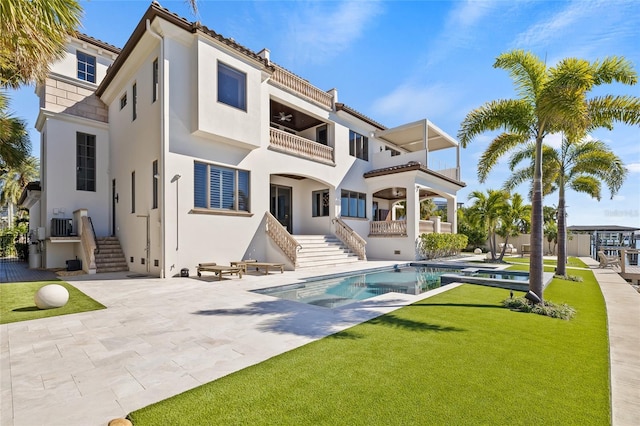 rear view of house with a yard, stucco siding, central AC unit, a patio area, and a balcony