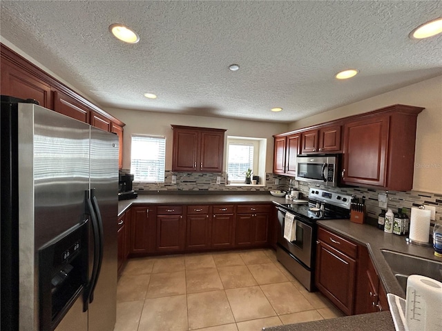 kitchen featuring stainless steel appliances, a wealth of natural light, dark countertops, and tasteful backsplash