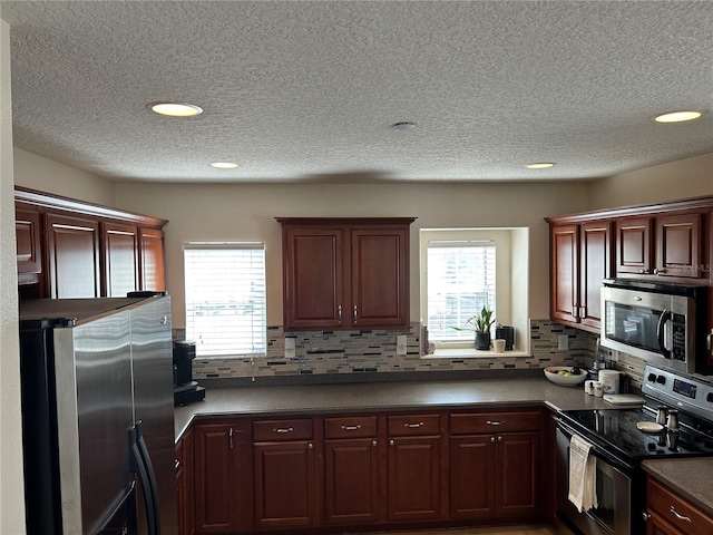 kitchen with appliances with stainless steel finishes, dark countertops, plenty of natural light, and backsplash