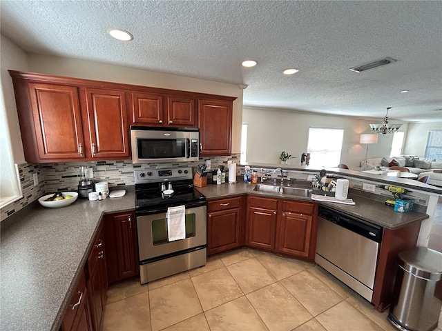 kitchen featuring stainless steel appliances, dark countertops, visible vents, a sink, and a peninsula