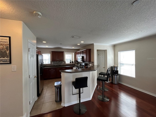 kitchen with a breakfast bar area, stainless steel appliances, a peninsula, backsplash, and dark countertops