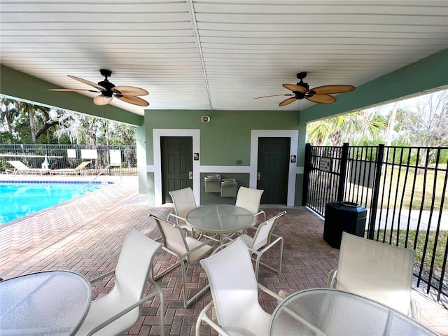 view of patio with outdoor dining area, fence, a community pool, and ceiling fan