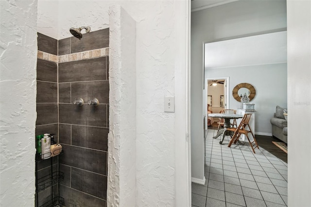 full bath featuring a textured wall, ceiling fan, tiled shower, baseboards, and tile patterned floors