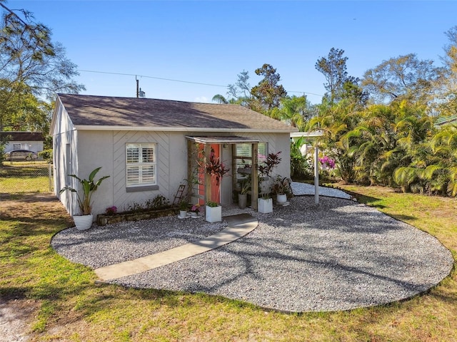 view of front of property with roof with shingles, fence, and stucco siding