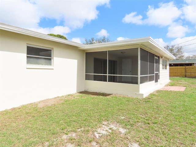 back of property with stucco siding, fence, a sunroom, and a yard