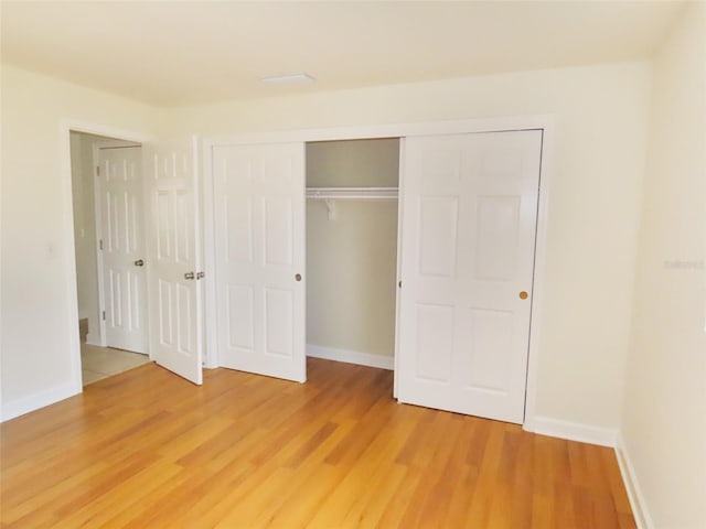 unfurnished bedroom featuring light wood-style flooring, baseboards, and a closet