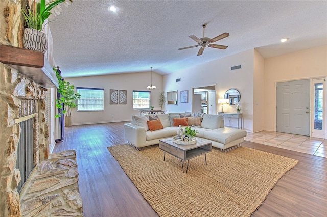 living room with a stone fireplace, visible vents, a textured ceiling, and wood finished floors