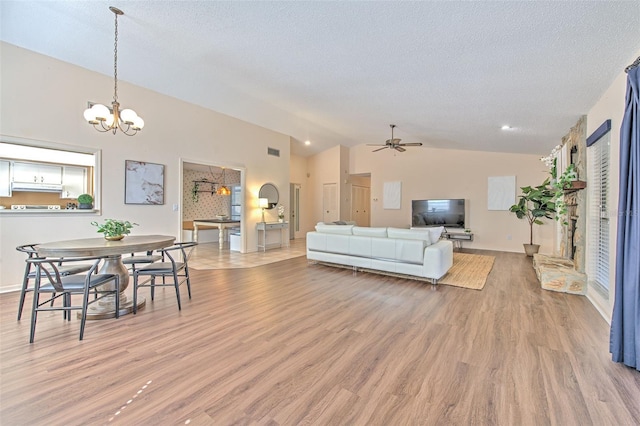 living room with a textured ceiling, ceiling fan with notable chandelier, visible vents, vaulted ceiling, and light wood finished floors