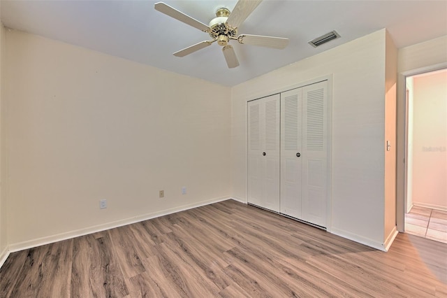 unfurnished bedroom with wood finished floors, a ceiling fan, visible vents, baseboards, and a closet