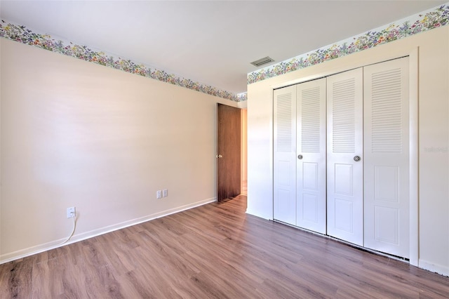 unfurnished bedroom featuring baseboards, a closet, visible vents, and wood finished floors