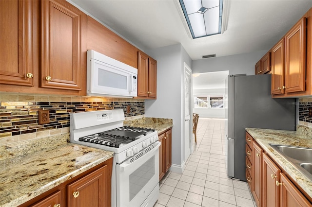 kitchen with white appliances, visible vents, brown cabinetry, and light tile patterned flooring