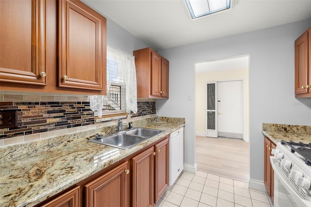 kitchen featuring light tile patterned floors, tasteful backsplash, brown cabinetry, a sink, and white appliances