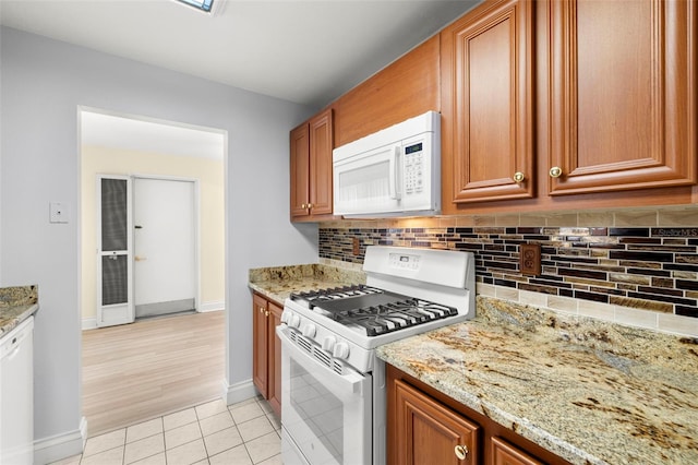 kitchen featuring brown cabinetry, white appliances, decorative backsplash, and light tile patterned floors