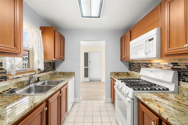 kitchen with white appliances, light tile patterned floors, decorative backsplash, brown cabinets, and a sink