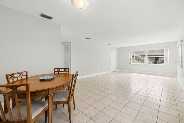 dining area featuring light tile patterned floors, baseboards, visible vents, and a textured ceiling