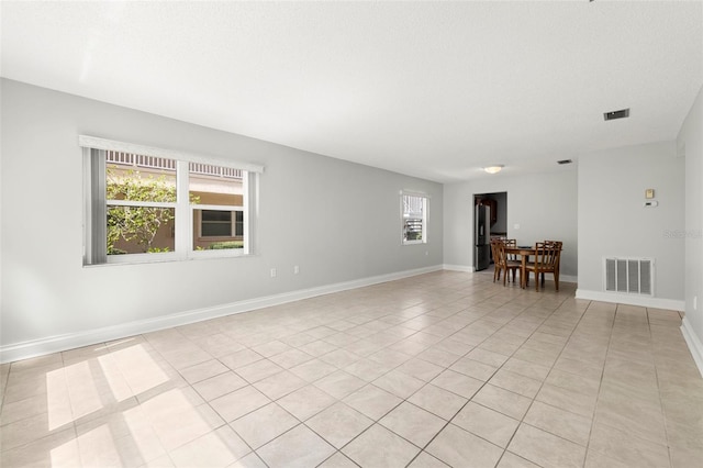 spare room featuring light tile patterned floors, a textured ceiling, visible vents, and baseboards