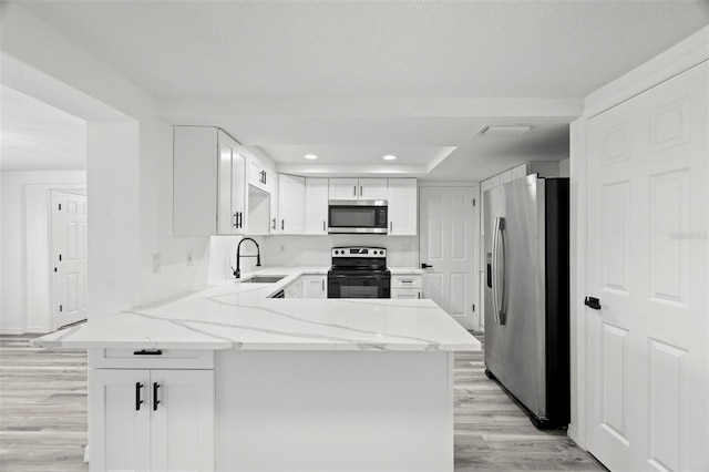 kitchen featuring a peninsula, a sink, appliances with stainless steel finishes, light wood-type flooring, and light stone countertops