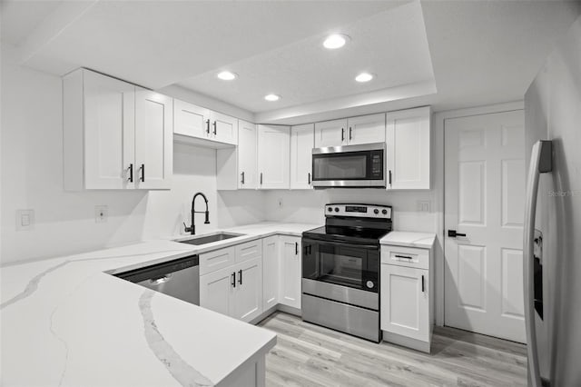 kitchen with appliances with stainless steel finishes, a sink, light wood-style flooring, and white cabinets