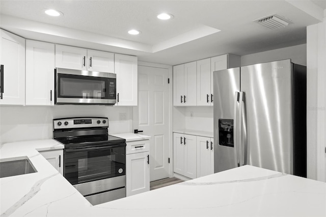 kitchen with stainless steel appliances, white cabinetry, visible vents, and light stone countertops