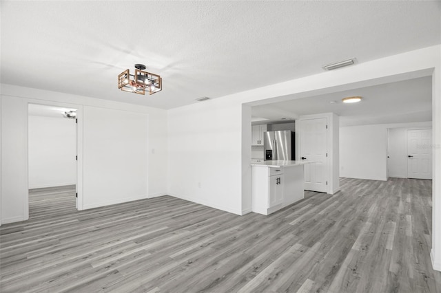 spare room featuring light wood finished floors, baseboards, visible vents, and a textured ceiling