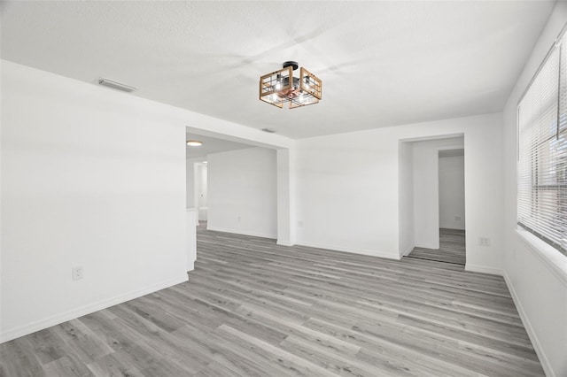 spare room featuring light wood-style floors, visible vents, a textured ceiling, and baseboards