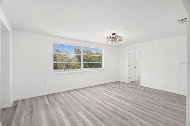 empty room with light wood-type flooring, baseboards, visible vents, and a textured ceiling