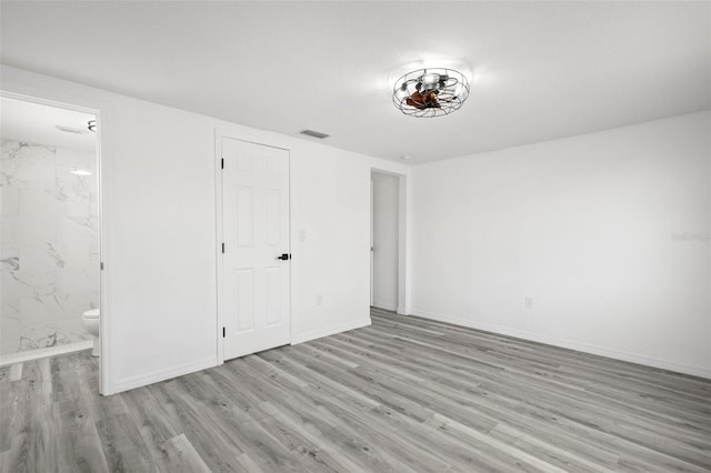 unfurnished bedroom with visible vents, connected bathroom, baseboards, and wood finished floors