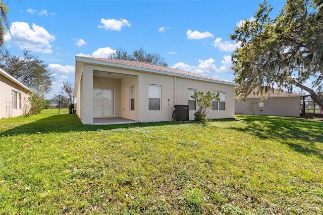 rear view of house with central air condition unit, a lawn, and stucco siding