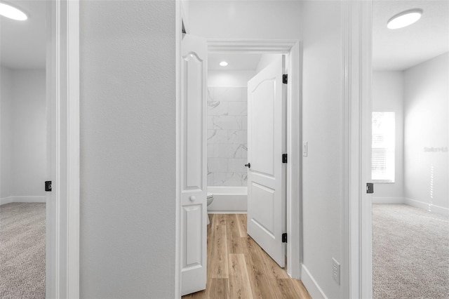 corridor with baseboards and light colored carpet