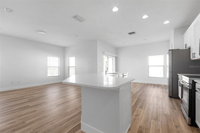 kitchen with light wood-style floors, stainless steel electric range oven, white cabinetry, and a sink