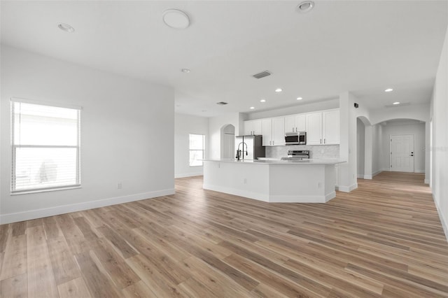 kitchen with tasteful backsplash, visible vents, arched walkways, stainless steel appliances, and white cabinetry