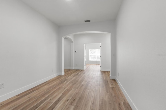 hallway with light wood-style floors, arched walkways, visible vents, and baseboards