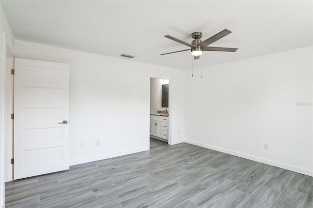 unfurnished bedroom featuring baseboards, visible vents, ensuite bath, light wood-style flooring, and ceiling fan