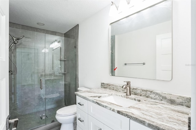 bathroom with a textured ceiling, a shower stall, toilet, and vanity