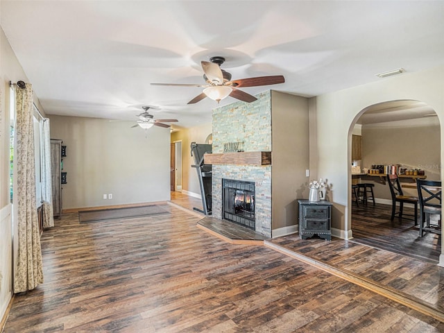 living room featuring arched walkways, a stone fireplace, wood finished floors, visible vents, and baseboards