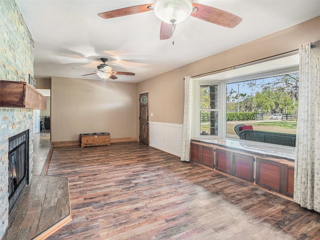 living room with a ceiling fan, a wainscoted wall, a fireplace, and wood finished floors