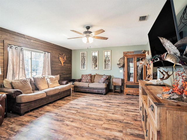 living room with a ceiling fan, visible vents, wood walls, and light wood finished floors